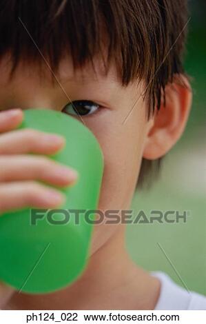 Stock Image - Young Asian boy drinking from cup, close-up. Fotosearch