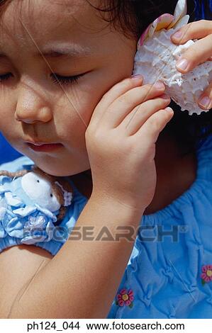 Young Asian girl holding a seashell close to her face, listening View Large Photo Image Picture - Young Asian girl holding a seashell close to her face, listening. Fotosearch