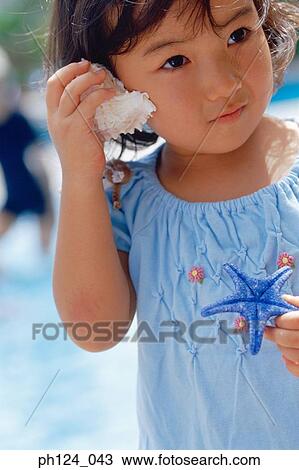 Young Asian girl holding a seashell close to her face View Large Photo Image Stock Image - Young Asian girl holding a seashell close to her face. Fotosearch