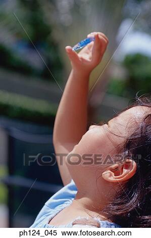 Stock Photography - Young Asian girl looking at blue plastic ornament against the sky. Fotosearch