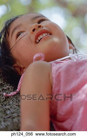 Stock Photograph - Young Asian girl resting on tree trunk, close-up. Fotosearch
