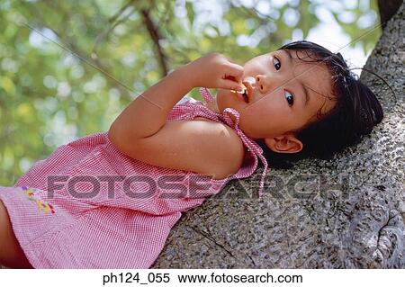 Stock Photography - Young Asian girl resting on tree trunk. Fotosearch