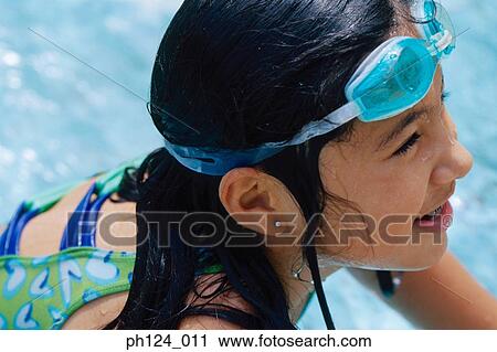 Stock Image - Young girl in the pool, swimming goggles on her head. Fotosearch