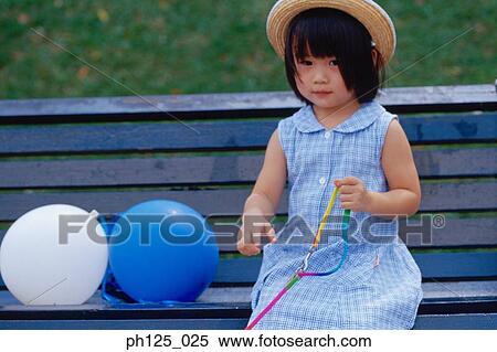 Stock Photography - Young Asian girl sitting on a bench with balloons. Fotosearch
