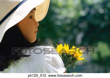 Stock Image - Young girl holding a stalk of sunflower. Fotosearch