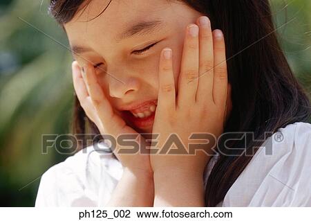 Stock Image - Young girl with her hands on her face, close-up. Fotosearch