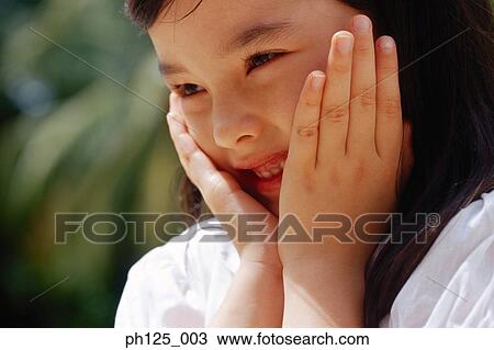 Stock Image - Young girl with her hands on her face, close-up. Fotosearch