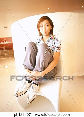 Stock Image - Portrait of a young woman, arms hugging her legs. Fotosearch