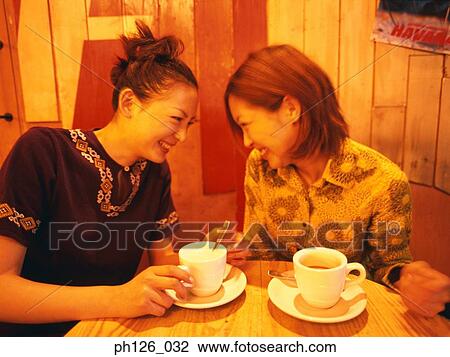 Stock Image - Two young women giggling at a café. Fotosearch