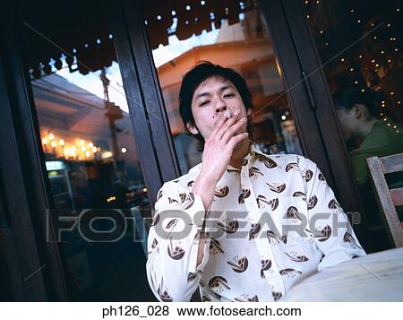 Stock Photo - Young man smoking outside sidewalk café. Fotosearch
