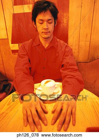 Young man with his eyes closed and a cup of cappuccino on the table View Large Photo Image Stock Photo - Young man with his eyes closed and a cup of cappuccino on the table. Fotosearch
