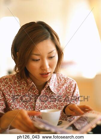 Stock Image - Young woman looking at photo album. Fotosearch