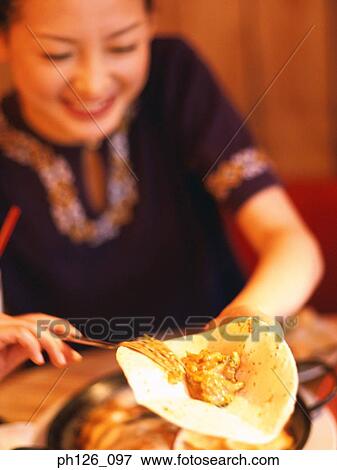 Stock Photo - Young woman spreading fillings on Fajita . Fotosearch
