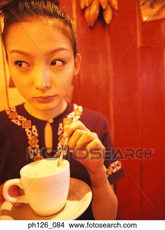 Young woman stirring a cup of coffee, looking away View Large Photo Image Picture - Young woman stirring a cup of coffee, looking away. Fotosearch