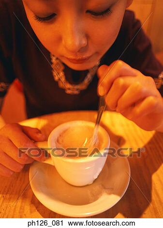 Stock Image - Young woman stirring a cup of coffee. Fotosearch