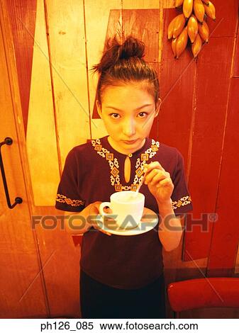 Young woman stirring a cup of coffee, looking at camera View Large Photo Image Stock Photography - Young woman stirring a cup of coffee, looking at camera. Fotosearch