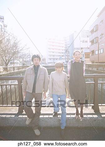 Stock Photo - Friends leaning against railing, sun shining from behind. Fotosearch