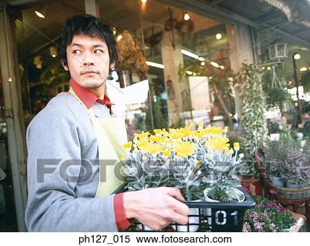 Stock Photography - Male florist carrying potted flowers, looking away. Fotosearch