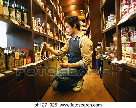 Stock Photography - Male store attendant replenishing grocery. Fotosearch