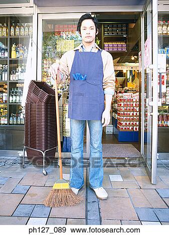Male store attendant standing outside a grocery store, holding a broom View Large Photo Image Stock Photo - Male store attendant standing outside a grocery store, holding a broom. Fotosearch