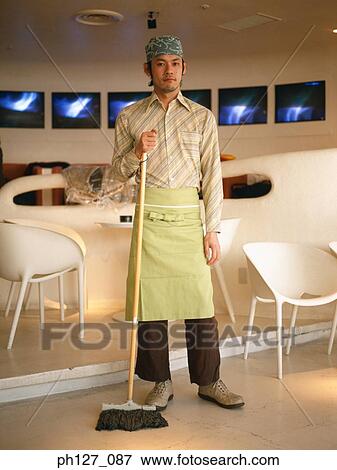 Male waiter standing at a café, holding a broom View Large Photo Image Stock Photo - Male waiter standing at a café, holding a broom. Fotosearch