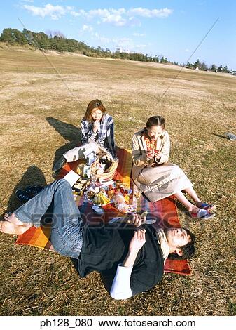 Three friends having picnic, young man lying on the ground View Large Photo Image Stock Image - Three friends having picnic, young man lying on the ground. Fotosearch