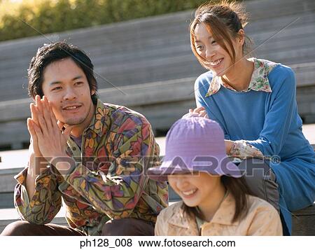 Stock Photo - Three friends sitting on steps, smiling. Fotosearch