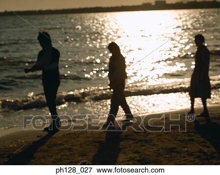 Stock Photo - Three people scrolling along the beach, silhouette. Fotosearch