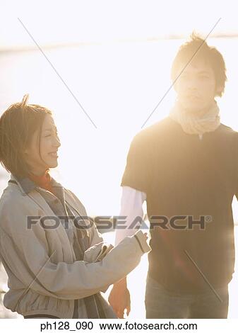 Stock Image - Young couple at the beach, sun shining from behind. Fotosearch