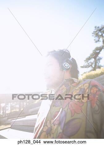 Young man listening to headphones, looking away View Large Photo Image Picture - Young man listening to headphones, looking away. Fotosearch