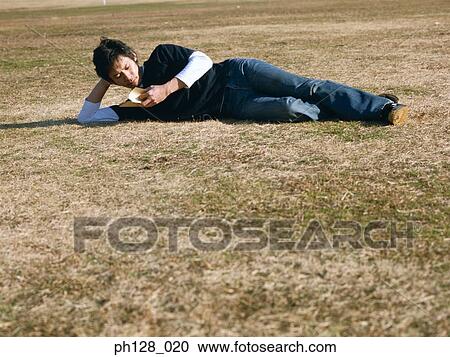 Young man lying on the field, reading View Large Photo Image Stock Image - Young man lying on the field, reading. Fotosearch