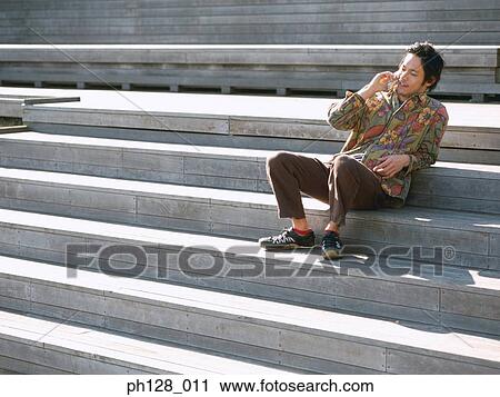 Young man sitting on steps, talking on mobile phone View Large Photo Image Stock Image - Young man sitting on steps, talking on mobile phone. Fotosearch
