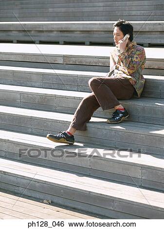 Young man sitting on steps, talking on mobile phone View Large Photo Image Stock Photograph - Young man sitting on steps, talking on mobile phone. Fotosearch