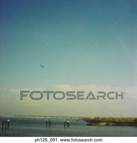 Stock Image - Airplane flying across the sea. Fotosearch