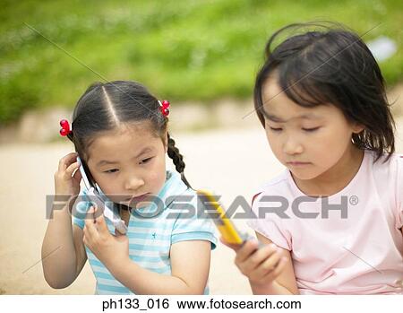 Stock Photograph - Two young girls talking using mobile phones. Fotosearch