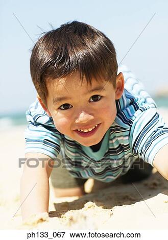 Stock Photo - Young boy lying in sand and smiling. Fotosearch