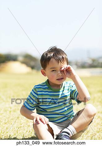 Stock Photo - Young boy sitting and rubbing eyes. Fotosearch