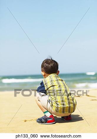 Young boy sitting on beach View Large Photo Image Stock Image - Young boy sitting on beach. Fotosearch