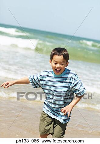 Stock Photograph - Young boy smiling & playing on beach. Fotosearch
