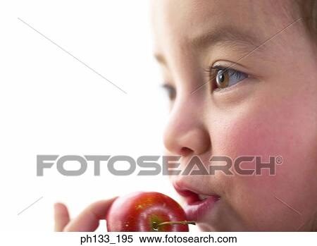 Stock Photography - Young girl holding a fruit up to her mouth. Fotosearch