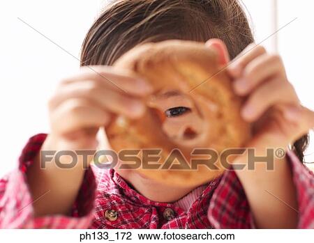 Stock Image - Young girl looking through a doughnut. Fotosearch