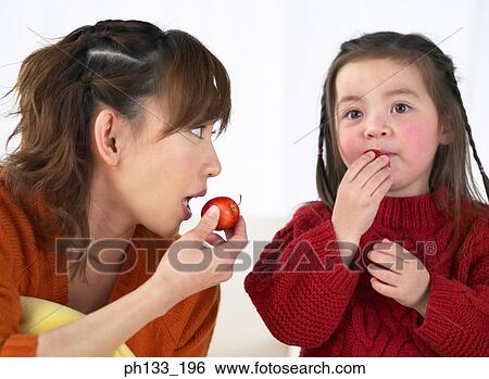 Stock Photograph - Young mother and daughter eating fruit. Fotosearch