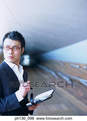 Stock Photo - Asian Man distracted from work. Fotosearch