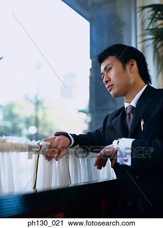 Stock Image - Asian Man looking out of a restaurant window. Fotosearch
