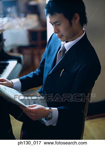 Stock Photo - Asian Man reading the papers by a piano. Fotosearch