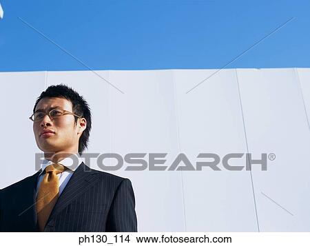Asian Man standing in front of a wall View Large Photo Image Picture - Asian Man standing in front of a wall. Fotosearch