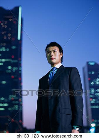 Stock Image - Asian Standing amidst skyscrapers. Fotosearch