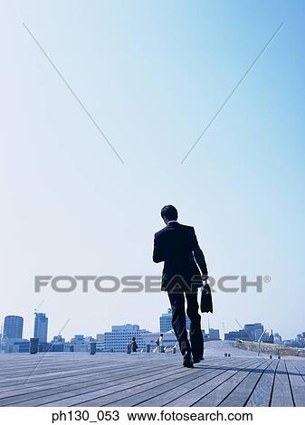 Stock Image - Back profile of a man walking on a bridge. Fotosearch