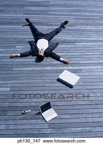 Stock Photo - Asian Man lying on a bridge with business accessories. Fotosearch