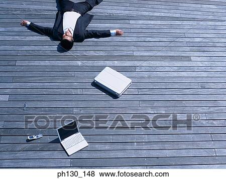 Stock Photo - Asian Man lying on a bridge with business accessories. Fotosearch